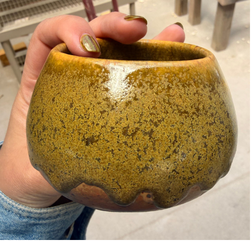 Small scalloped cup with a mottled ochre glaze, held in hand.