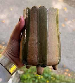 Faceted footed tumbler with a green ash glaze, held in hand outdoors.
