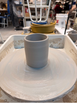 A freshly thrown clay cylinder centered on the pottery wheel in the studio.